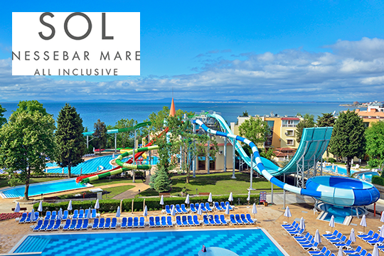 Blick über Hotelanlage mit Pool und Wasserrutschen, im Hintergrund das Meer